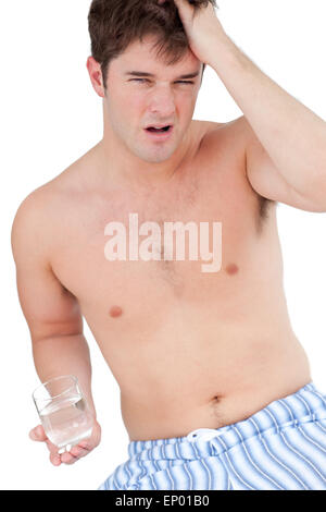 L'homme épuisé dans pajamas holding un verre d'eau, regardant la caméra sur un fond blanc. Banque D'Images