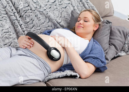 Jeune femme mettant ses écouteurs sur son ventre Banque D'Images