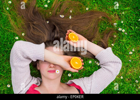 Young woman laying on a grass field holding oranges Banque D'Images