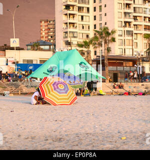 Les jeunes gens assis sous un parasol couché sur le côté sur la plage de Cavancha beach à Iquique, Chili Banque D'Images