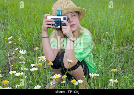 Petite fille avec appareil photo rétro dans un champ de marguerites. Banque D'Images