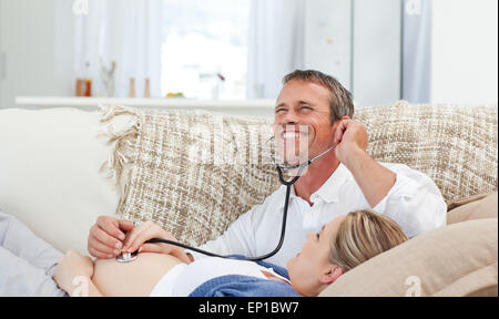 L'homme écoute le ventre de sa femme avec son stéthoscope Banque D'Images