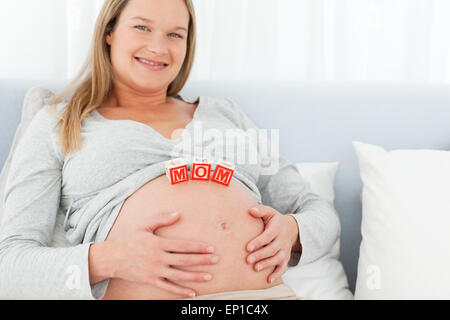 Blonde femme enceinte avec maman lettres sur son ventre couché sur un lit Banque D'Images