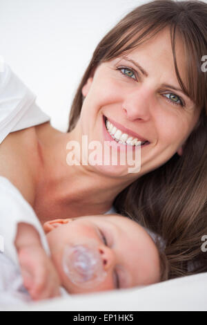 Smiling brunette woman lying pendant que son bébé dort Banque D'Images