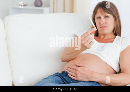 Charmante femme enceinte tenant une cigarette tout en se trouvant sur un canapé Banque D'Images