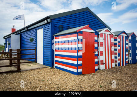 Une ligne de red, white and blue striped cabanes de plage à côté d'un grand hangar en bois bleu Banque D'Images