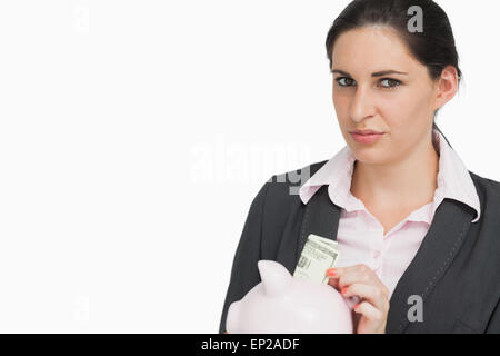 Brunette woman mettant l'argent dans un piggy-bank Banque D'Images