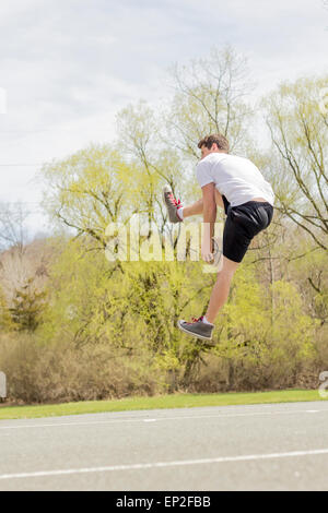 Jeune homme faisant le basket Trick Shots comme il saute en l'air Banque D'Images