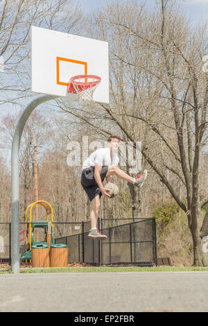 Jeune homme faisant le basket Trick Shots comme il saute en l'air Banque D'Images