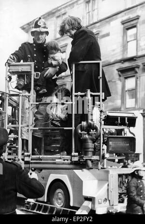 Incendie à Maryhill Road Glasgow. Feu dans un magasin de meubles inoccupés se propager le long de la rangée de boutiques et de piégeage des familles dans leurs maisons ci-dessus. Cinquante familles sont sans abri et d'une femme et d'un officier pompier ont perdu la vie. Samedi, 18 novembre 1972. Sur la photo, John Mathieson qui a sauvé deux enfants de l'incendie. Isobel âgés de 3 est détenu par un pompier et Robert de 4'accroche à la jambe de Mathieson. Banque D'Images