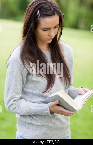 Une jeune femme lisant un livre tout en se tenant dans un parc Banque D'Images