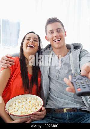 Un rire couple assis sur le canapé avec le pop-corn qu'ils regardent la télévision Banque D'Images