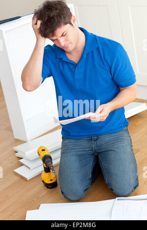 Jeune homme Incomprehensive lire les instructions d'assemblage de meubles dans la cuisine à la maison Banque D'Images