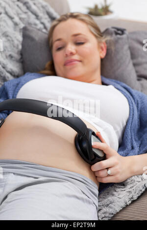 Jeune femme mettant ses écouteurs sur son ventre Banque D'Images