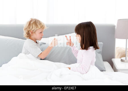 Frère et sœur jouant mignon pierre papier ciseaux et sur le lit des parents Banque D'Images