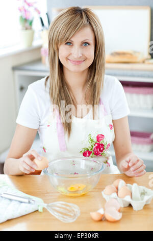 Femme joyeuse la cuisson dans la cuisine et casser des œufs Banque D'Images