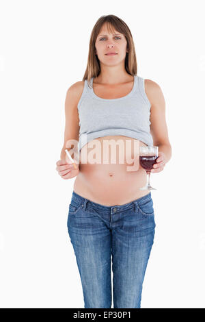 Belle femme enceinte tenant un verre de vin rouge en position debout Banque D'Images