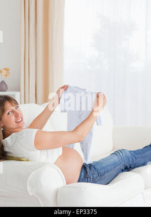 Jolie femme enceinte tenant un bébé grandir et posing while sitting on a sofa Banque D'Images