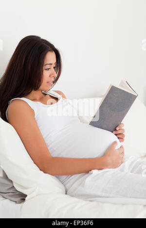 Charmante femme enceinte lire un livre tout en étant allongé sur un lit Banque D'Images