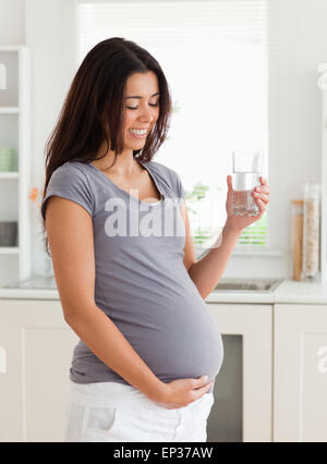 Charmante femme enceinte tenant un verre d'eau en position debout Banque D'Images