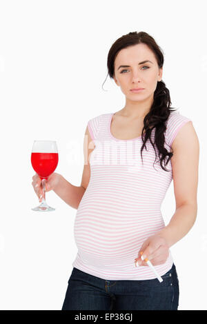 Jeune femme enceinte holding alcoholic drink and cigarette Banque D'Images