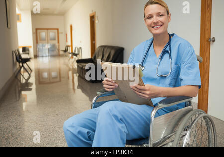 Smiling nurse in a wheelchair holding un dossier Banque D'Images