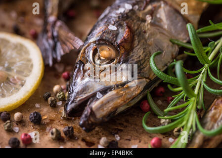 Du poisson cuit au four avec des épices, le citron et le romarin sur un pan de grillage avec papier cuisson Banque D'Images