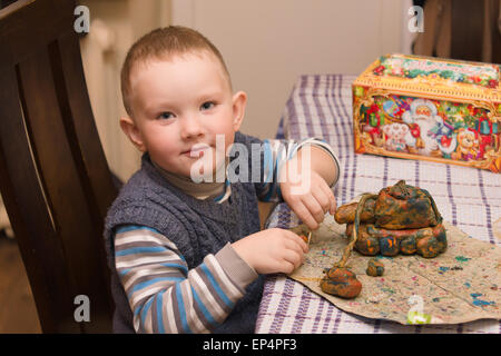 Le petit garçon est assis à une table et produits de moules de la pâte à modeler Banque D'Images