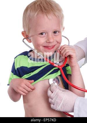 Médecin examine un jeune enfant. boy est à l'écoute de son propre coeur avec son stéthoscope. Il aide médecin par ascenseur sa chemise en place. Banque D'Images