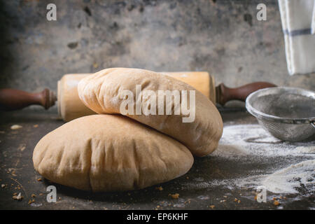 Deux de farine de pain de pita sur planche à découper en bois, servi avec du matériel roulant vintage broches et la farine sur la table sombre Banque D'Images