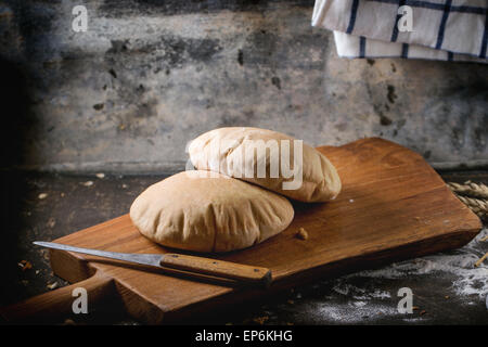 Deux de farine de pain de pita sur planche à découper en bois, servi avec le couteau et la farine sur la table sombre Banque D'Images