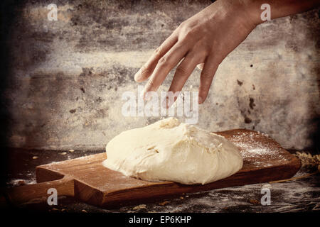 La main de l'homme de la poudre avec la farine la pâte à pizza sur une planche à découper en bois foncé sur table de cuisine. En effet filtre rétro Banque D'Images