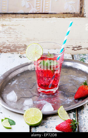 Verre à cocktail rétro avec tubes limonade aux fraises fait maison, servi avec des fraises fraîches, menthe, citron vert et des glaçons sur Banque D'Images