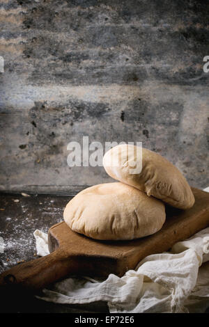 Deux de farine de pain de pita sur planche à découper en bois, servi avec de la farine sur la table sombre Banque D'Images