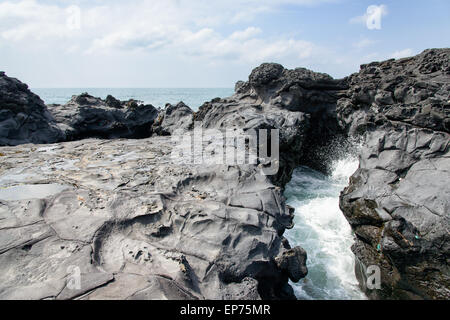 Paysage avec jet d'eau par l'eau de mer a frappé par tunnel entre des pierres sur la côte près de la route 16 en piste Olle Jeju Banque D'Images