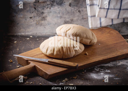 Deux de farine de pain de pita sur planche à découper en bois, servi avec le couteau et la farine sur la table sombre Banque D'Images