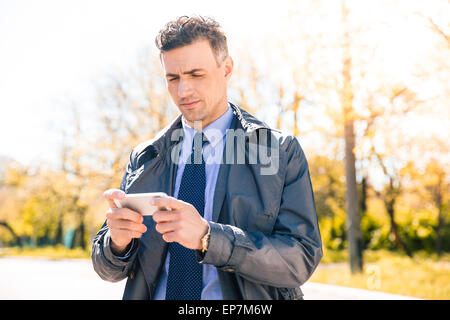 Confident businessman in suit en utilisant smartphone outdoors Banque D'Images