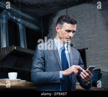 De graves handsome businessman using smartphone in cafe Banque D'Images