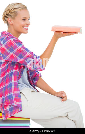 Belle femme montrant un livre et assis sur une pile de livres Banque D'Images