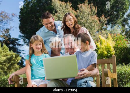 Smiling multi generation family with a laptop sitting in park Banque D'Images