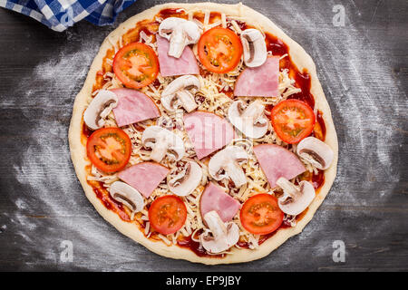 Fabrication de pizzas. Sauce, le fromage, les champignons, le jambon et les tomates sur une pâte Banque D'Images