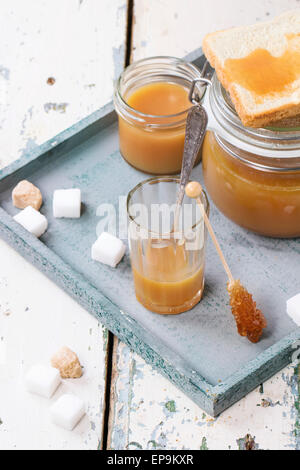 Pot de sauce au caramel fait maison, servi avec des morceaux de sucre sur la table en bois Banque D'Images