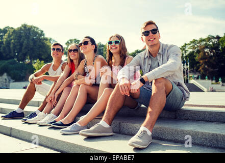 Group of smiling friends sitting on city street Banque D'Images