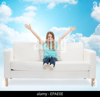 Happy girl sitting on sofa avec main levée Banque D'Images