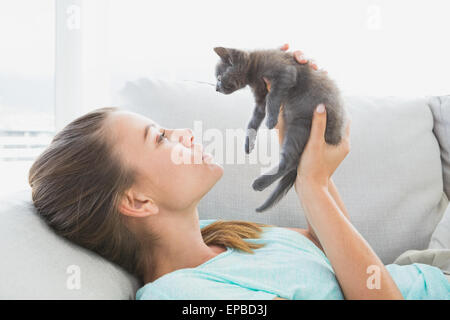 Cheerful woman lying on sofa holding un chaton gris Banque D'Images