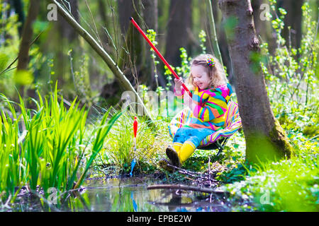 Enfant jouant à l'extérieur. Enfant d'âge préscolaire la capture de poissons avec tige rouge. Petite fille de la pêche dans la rivière de la forêt en été. Banque D'Images