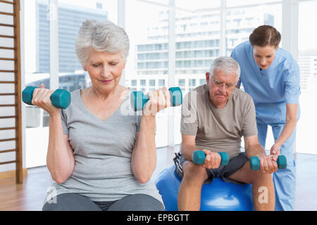 Female therapist aider senior couple with dumbbells Banque D'Images