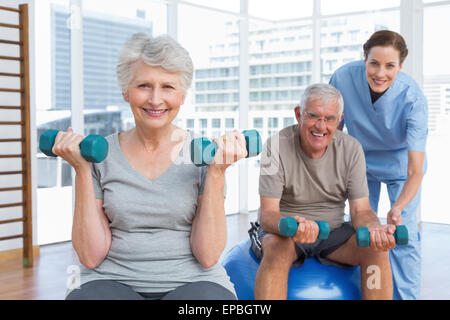 Female therapist aider senior couple with dumbbells Banque D'Images