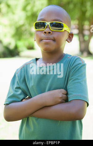 Petit garçon en lunettes de soleil avec les bras croisés Banque D'Images