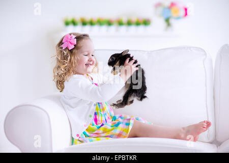 Heureux rire petite fille jouant avec un bébé lapin, serrant son vrai bunny pet et apprendre à prendre soin d'un animal Banque D'Images